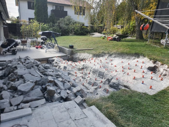 Berg som hydrauliskt spräckts i trädgård med högar av sprängsten och markeringspinnar.