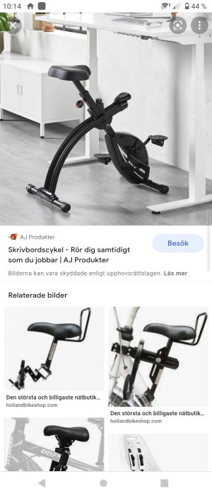 Svart kompakt skrivbordscykel placerad framför ett vitt skrivbord i en ljus inredning.