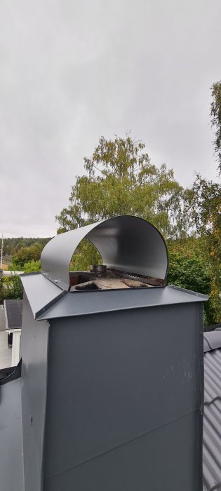 Skorsten med monterad solbåge före renovering, med träd och himmel i bakgrunden.