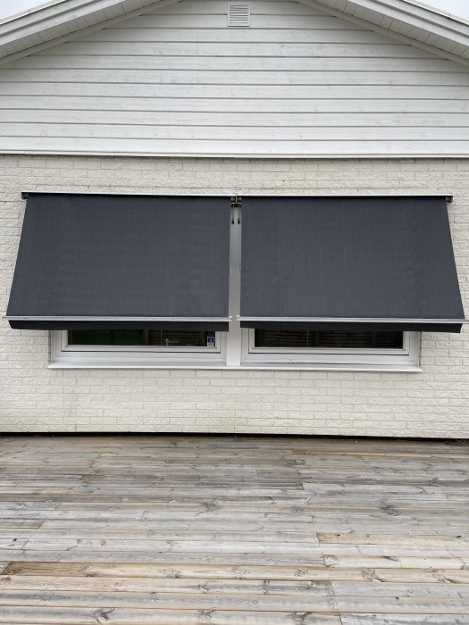 Ny svart markisväv installerad på vit husfasad ovanför fönster med träterrass i förgrunden.