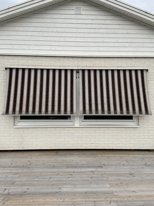 Nya markisvävar med brunrandigt mönster installerade på ett vitt hus med två fönster.