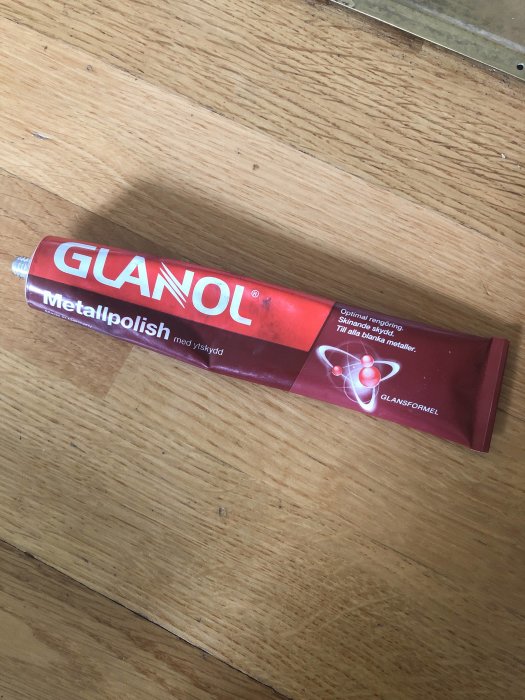 Tub med Glanol metallpolish på ett trägolv, använd för att polera dörrar.