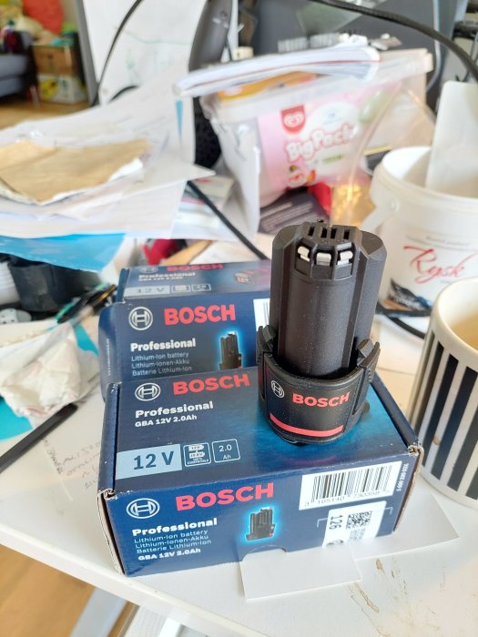 Bosch 12V 2.0Ah lithium-ion batterier på skrivbord med rörig bakgrund.