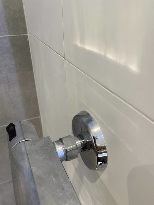 Närbild på en silverfärgad duschblandarfäste mot en kaklad badrumsvägg.