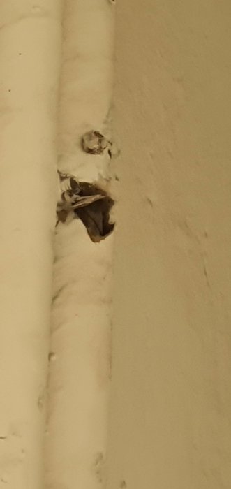 Skadad isolering på värmerör med misstänkt asbest i böj, vägg i bakgrunden.