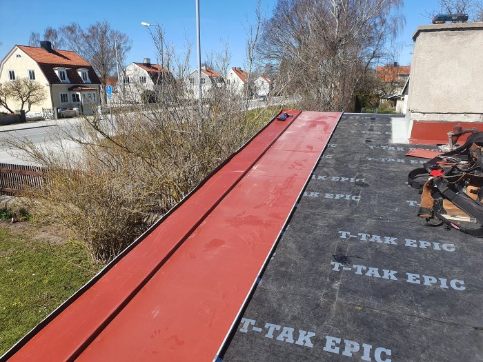 Röd bandfalsad takplåt som delvis är installerad på ett hus under soligt väder.