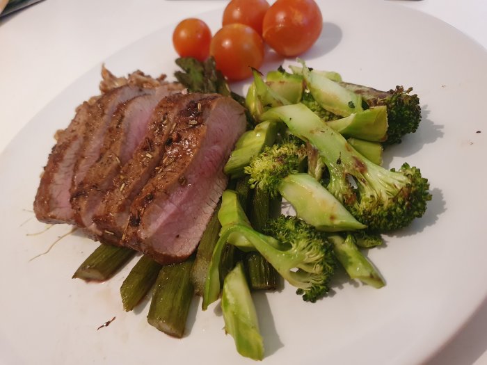 Lammytterfilé skivad på tallrik med broccoli, sparris och körsbärstomater.