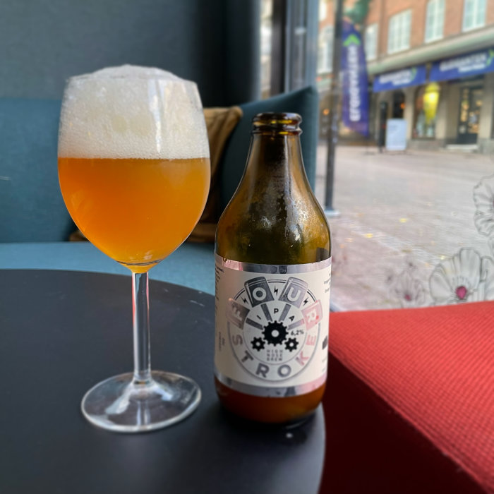 Ett glas med öl och en halvtom flaska med etikett mot en stadsgata.