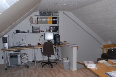 Vind med kontorssetup, datorterminal, och förberedelse för takkupa innan renovering.