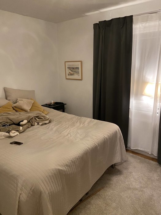 Sovrum med en opersonlig inredning, vitmålade betongväggar, tunga mörkläggningsgardiner och en tjock matta.