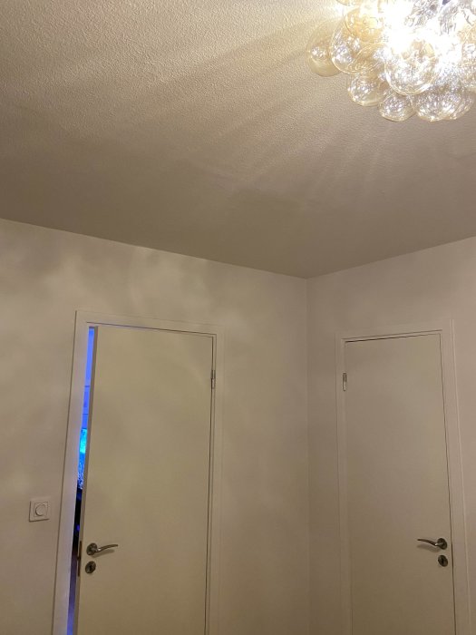 Oinredd sovrumsinteriör med släta betongväggar, två vita dörrar och en takkrona.