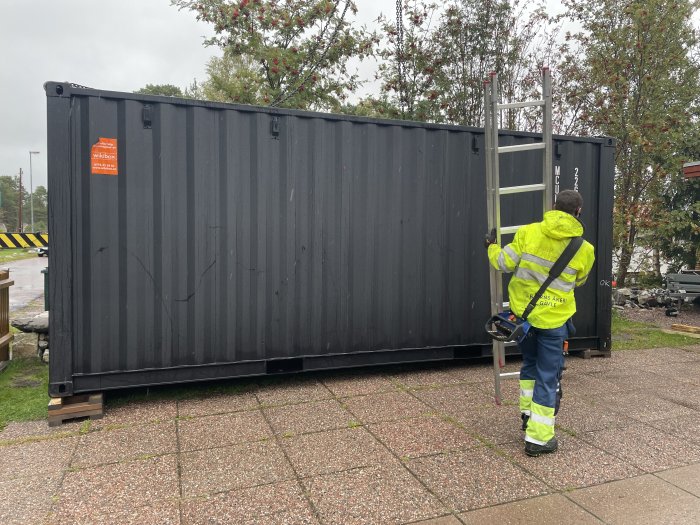 Person i reflexjacka står bredvid en ny, svart container som är isolerad.