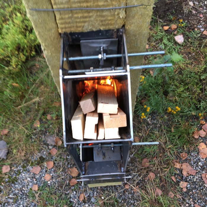 Hemmagjord asklåda med brinnande ved och öppen luftspjällsreglering.