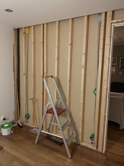 Avlägsnade väggskivor avslöjar träreglar och installationer bakom, med stege framför i ett rum under renovering.