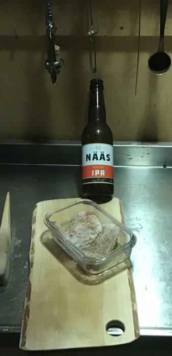 Kycklingfile kryddad med salt och peppar i genomskinlig skål bredvid en flaska Naäs IPA på en skärbräda.