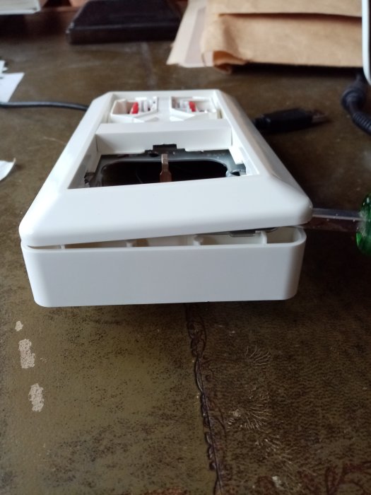 Skruvmejsel som bänder på en vit plasteluttagram på ett bord, indikerande försök att montera loss den.