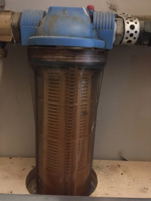 Vattenfilter med blåa detaljer och slitage som läcker vatten i källaren.