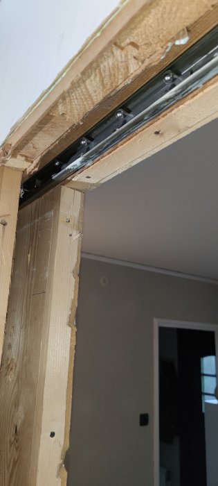 Öppning i vägg där en metallskena för en skjutdörr är monterad i sidan, synliga trästöd och oskyddad balk.