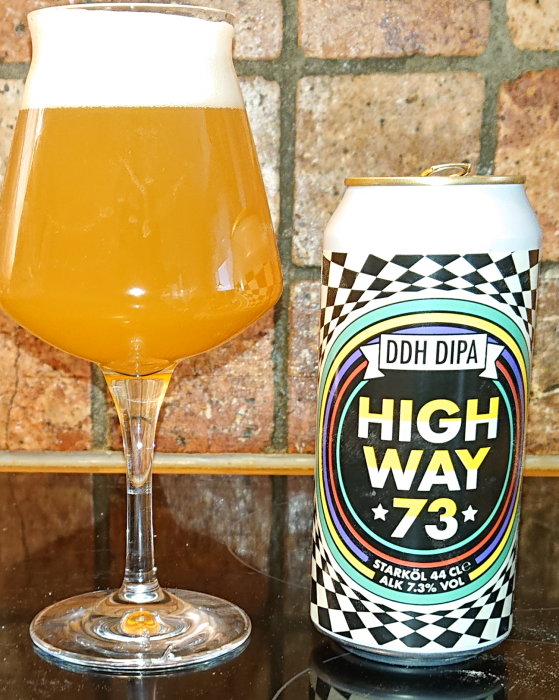 Ölglas fyllt med grumlig öl bredvid en burk märkt "DDH DIPA HIGHWAY 73" på tegelbakgrund.