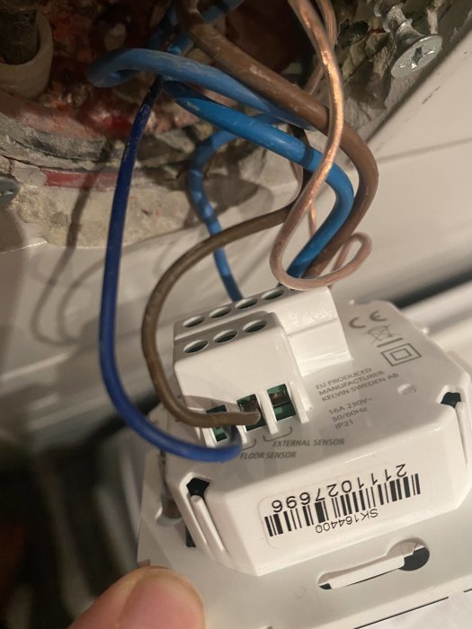 Elektrisk golvsensordosa med anslutna kopparledningar och blå kablar i ett öppet väggutrymme.