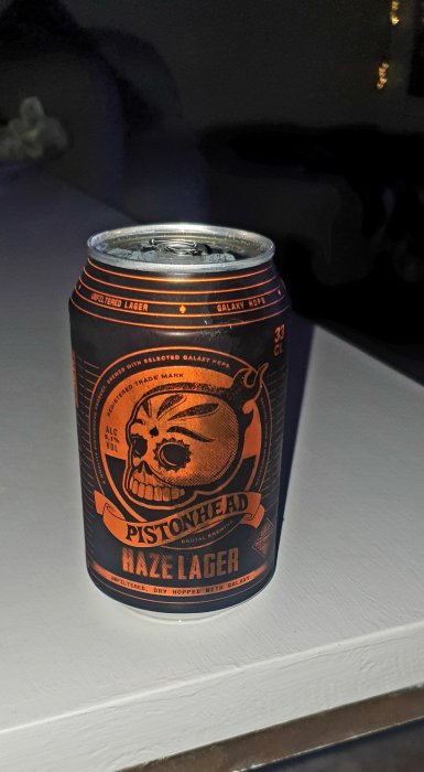 Burk med Pistonhead Haze Lager öl placerad på en yta, mörk bakgrund, framhäver burkens design.
