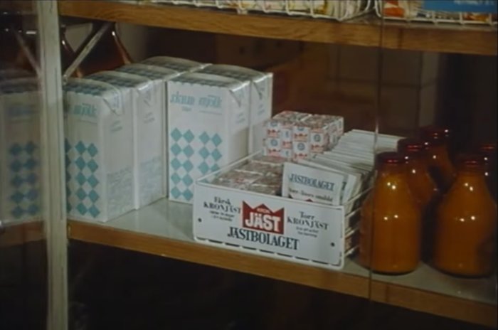 Mjölkpaket och bruna glasflaskor på trähyllor från 1960-talet.