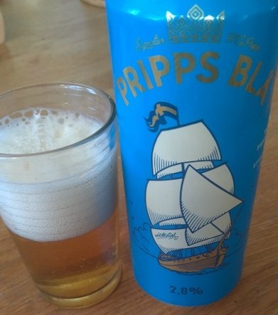 Ett glas med öl bredvid en blå ölburk med etikett "Pripps Blå" och en segelbåtsteckning.