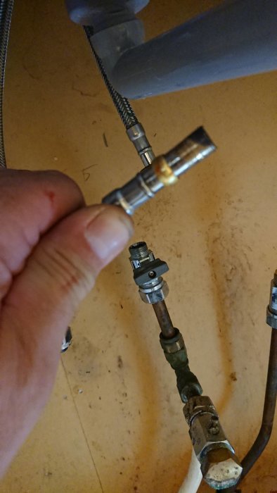 Hand som håller en klämring och mutter nära ett kallvattenrör och balofix ventil under installation.