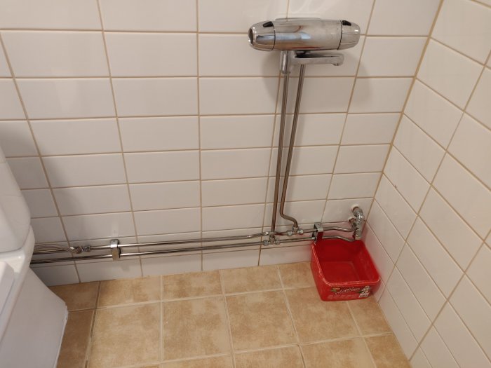 Monterad badkarsblandare och vägganslutna rör med ett rött verktygslåda i en kaklad badrumsmiljö.