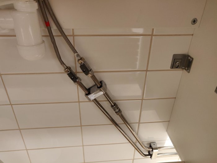 Installation av badkarsblandare med rör och kopplingar på vit kakelvägg.