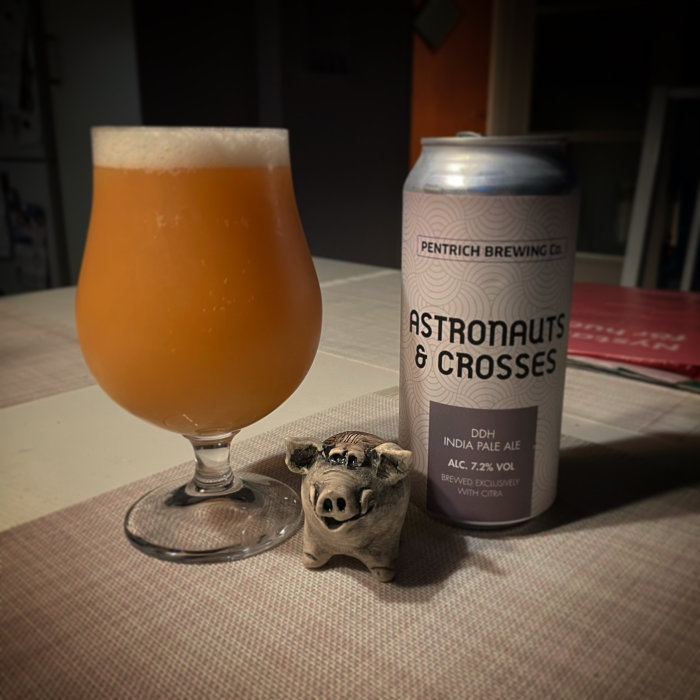 Ölglas fyllt med grumlig öl bredvid en ölburk och en liten figur av en gris.