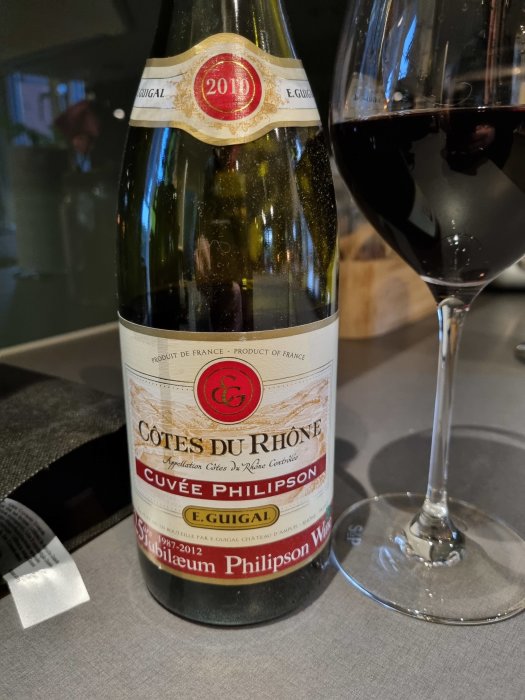 Flaska av 2010 Cuvée Philipson Côtes du Rhône Guigal nära ett glas rött vin.