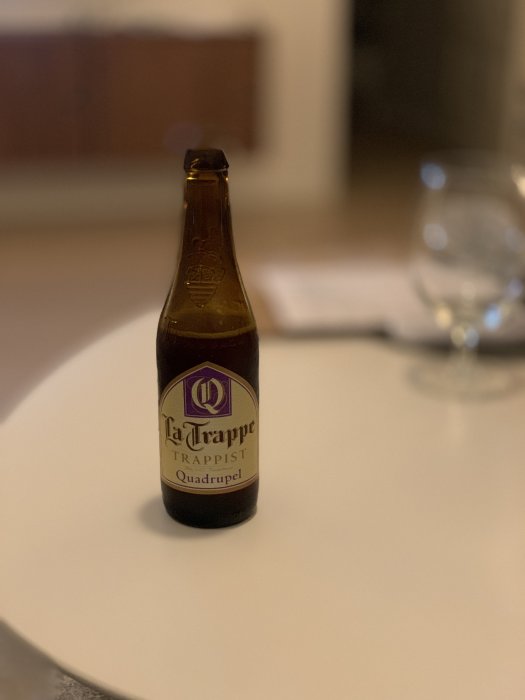 Flaska av La Trappe Trappist Quadrupel öl på ett bord, oskarp bakgrund.