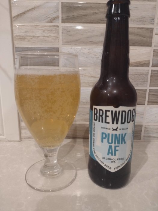 En flaska Brewdog alkoholfri öl bredvid ett glas fyllt med öl på köksbänk.