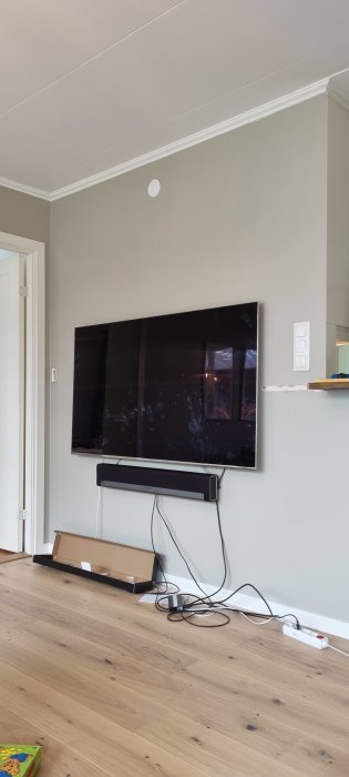 TV och soundbar på vägg med synliga elkablar och grenuttag på golvet.