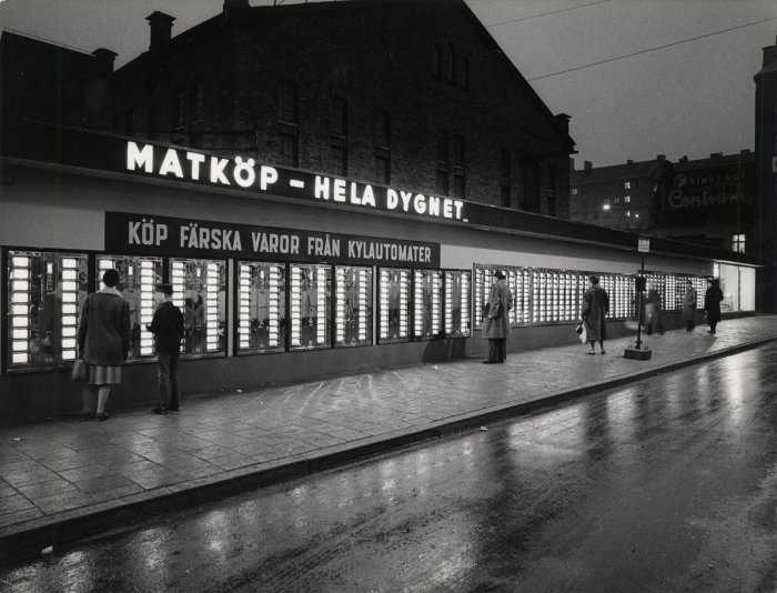 Svartvit bild av världens största varuautomat på Götgatan i Stockholm med människor som köper varor.