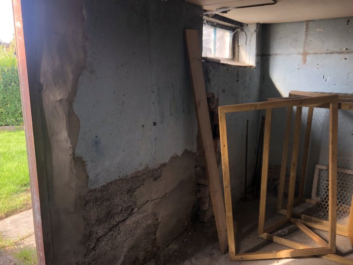 Gammalt pannrum under renovering med synlig betongvägg, jordyta och träram vid ett fönster.