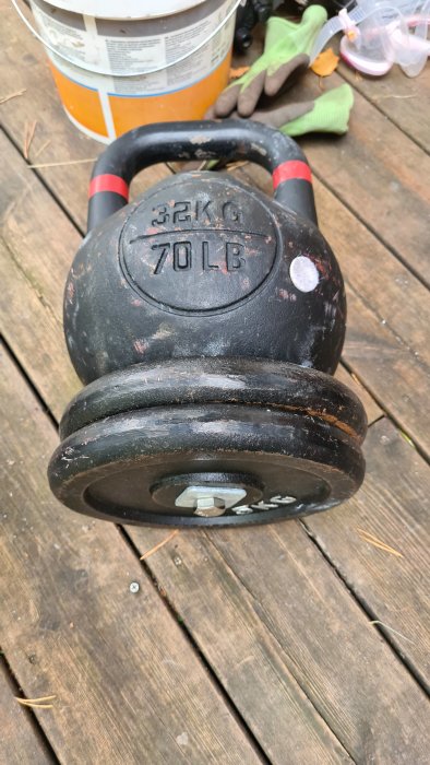 32kg kettlebell med skruvat extravigt på undersidan liggande på trägolv bredvid träningshandskar.