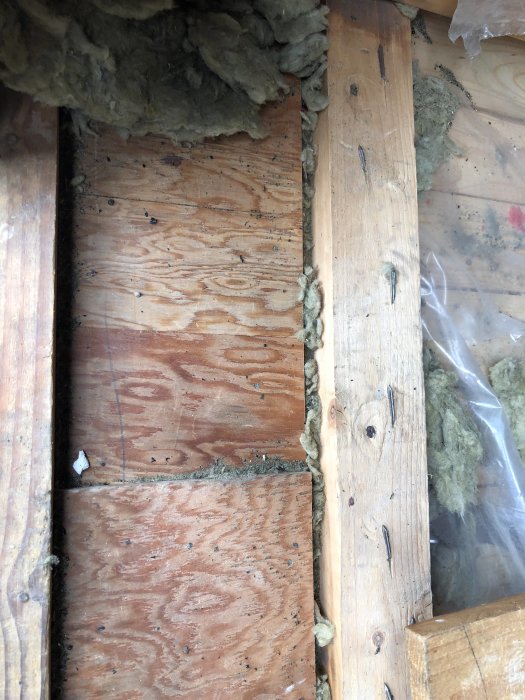 Närbild på en delvis avtäckt plywood i golvkonstruktion med isoleringsmaterial synligt vid kanterna.