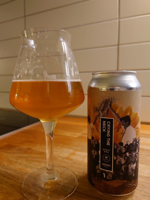 Ölglas fyllt med bärnstensfärgad öl bredvid en ölburk med etikett "Crying The Neck" från Verdant.