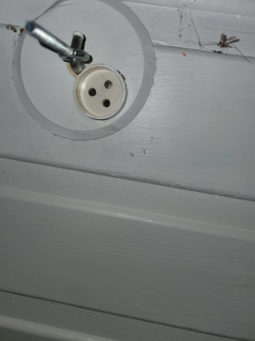 Enkel upphängning för lampa på vitmålat tak med synliga kablar och dammsamlare.