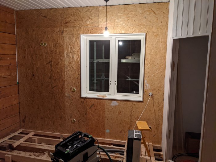 Vägg med OSB-skivor, nymålad fönstersmyg och grundat skafferi i en under renovering.