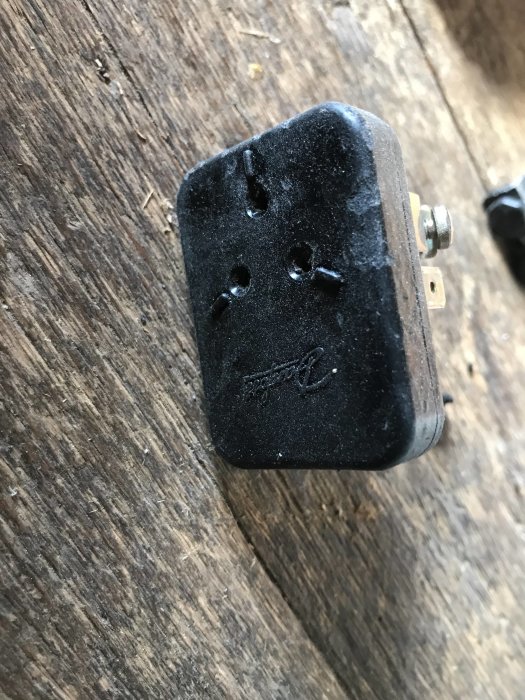 Svart relä med tecken på skada på en träyta, möjlig överbelastning eller defekt.
