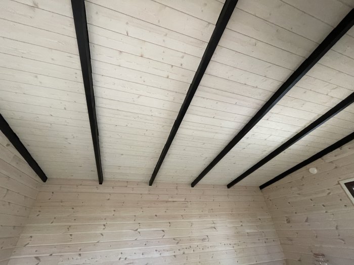 Interiör med vitlaserade träpaneler på vägg och tak som uppvisar färgskiftningar.