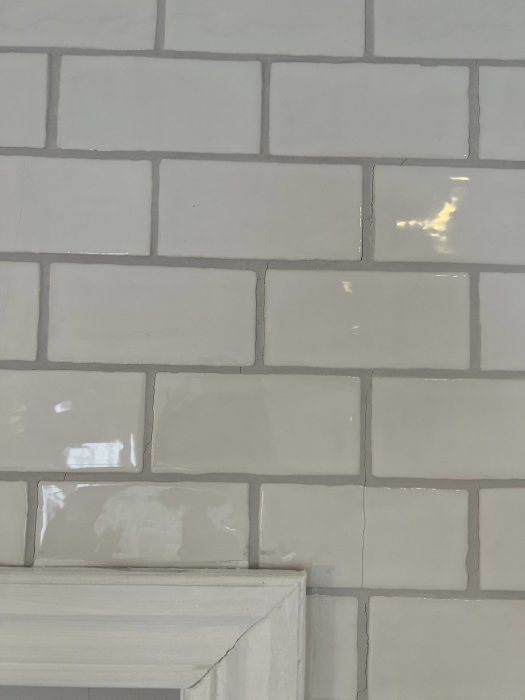 Kakelvägg med spruckna plattor och skadad fog, tecken på möjlig sättning i byggnaden.