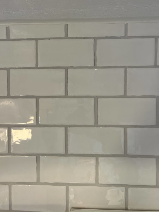 Vägg med kakelplattor, flera med sprickor och skadade fogar, indikerar möjlig sättning i byggnaden.