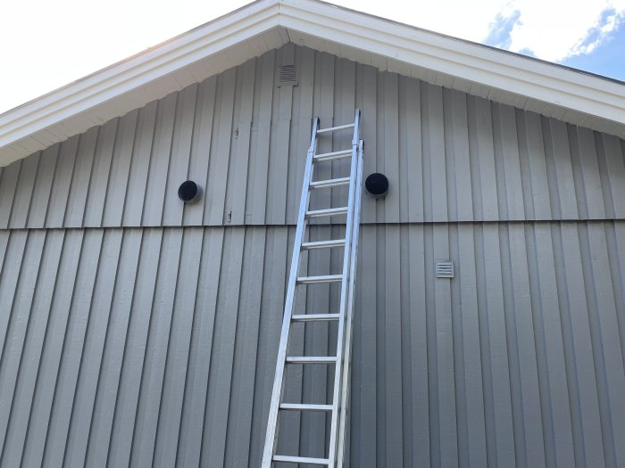 Husgavel med två ventilationsrör och en stege lutad mot väggen.