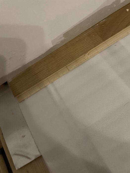 En bit parkettgolv intill en vit vägg, där golvbrädorna behöver tas bort nära golvärmerör.