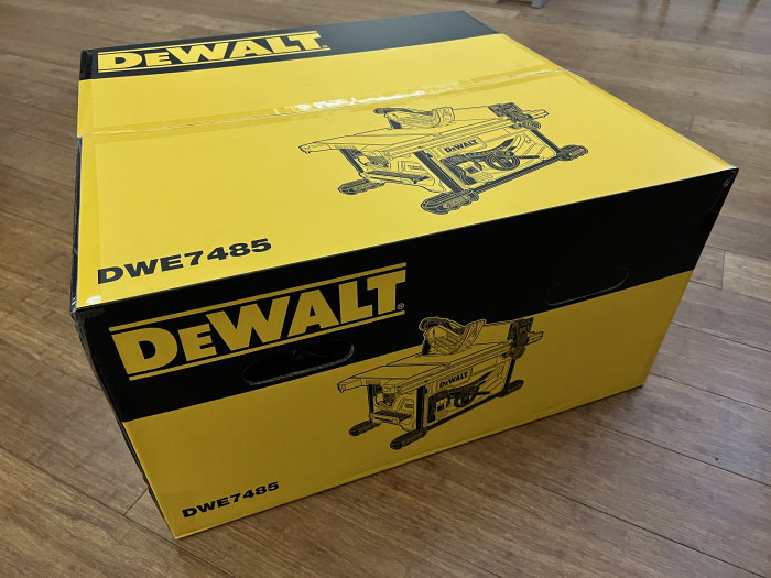 Förpackningen till en ny Dewalt bordsåg, modell DWE7485, på ett trägolv.