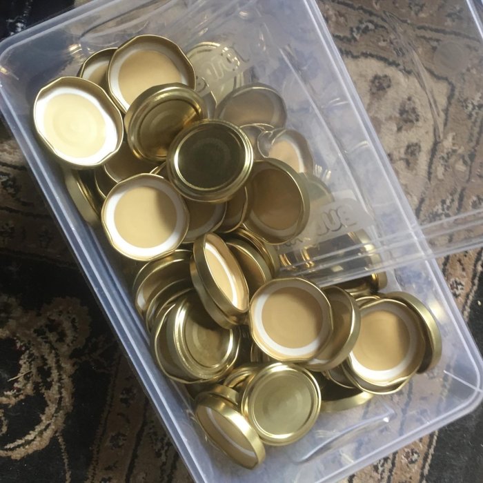 En plastlåda fylld med guldiga lock ordnade och sorterade för flaskor eller burkar.